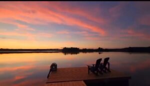 Beautiful photo looking out on the lake from the dock at sun set with a bright pink sky also reflected in the water.